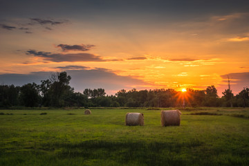 Sunset over the meadow and bales of straw