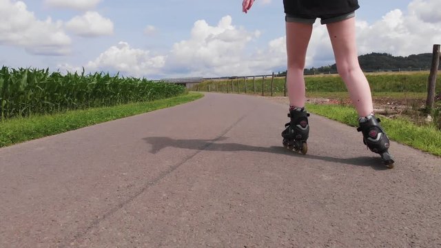 handheld drone follow shot of an red haired woman who is inline skating between corn fields in nature with main focus on skates