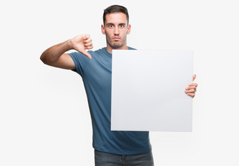 Handsome young man holding advertising banner with angry face, negative sign showing dislike with...