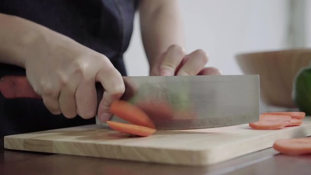 Close up of chief woman making salad healthy food and chopping carrot on cutting board in the kitchen.