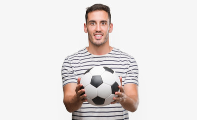 Handsome young man holding soccer football with a happy face standing and smiling with a confident smile showing teeth