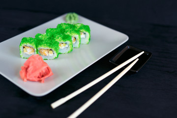 Rolls on a white plate on a black background with ginger and vassabi