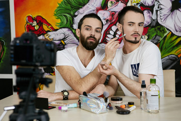 2 handsome young vloggers filming male makeup tutorials for a youtube channel, looking at the...