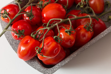 Pomodori freschi maturi su gambo dentro a contenitore grigio