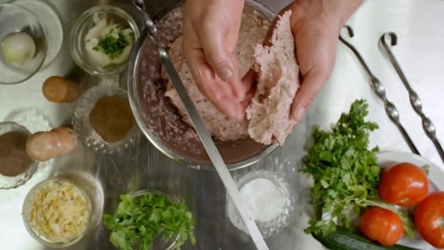 Top view of male hands forming ground meat and spreading it over metal skewer while forming lula kebab