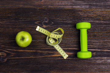 Green dumbbel, green apple and measuring tape on wooden background. Sport, fitness and diet concept.