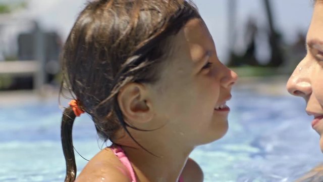 Closeup of happy little girl laughing and smiling while chilling in swimming pool with mother at hot summer day