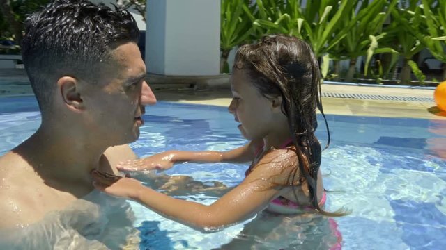 Loving dad speaking with little daughter while chilling in swimming pool and hot sunny day on vacation