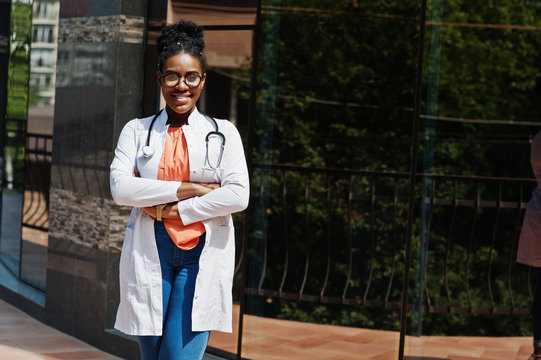 African american doctor female at lab coat, glasses with stethoscope posed outdoor against clinic.