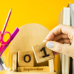 A female hand puts a cube with the date of September 1 on a wooden calendar. Among textbooks and...