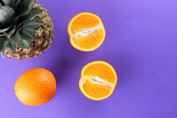 Pineapple and oranges on a purple background, citrus top view, pineapple and halves of oranges in...