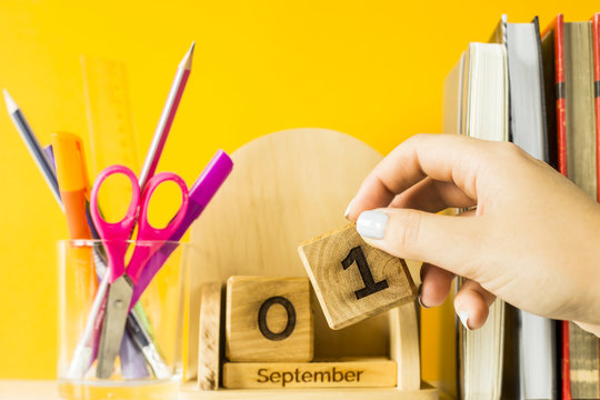 A female hand puts a cube with the date of September 1 on a wooden calendar. Among textbooks and pens for study. Back to school concept