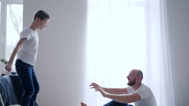young father catches son and then tickles him on bed and have fun playing at home in slow motion