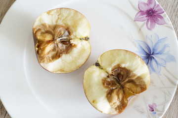 Rotten apple served on a white plate sliced in half