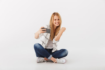 Obraz na płótnie Canvas Portrait of cheerful young casual girl looking at mobile phone