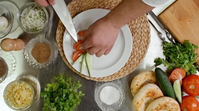 Top view fast motion of hands of restaurant chef serving lula kebab on white plate with fresh tomato, cucumber, quick pickled onion and bun on side