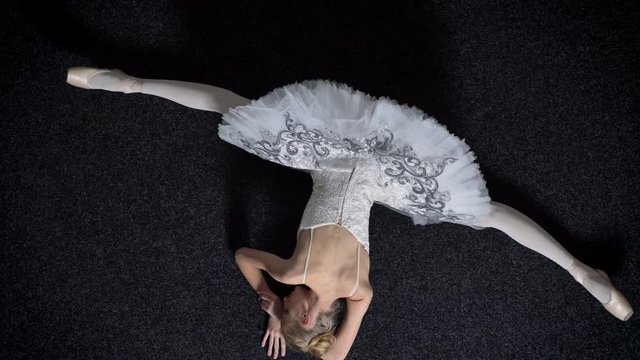 Silhouette of young girl ballerina is sitting on floor, stretching on splits, ballet concept, top shot