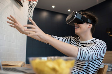 Excited teenager extending hands forward while using virtual reality headset sitting at home