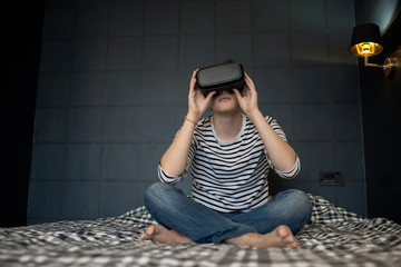 Teenager using virtual reality while sitting on bed in dark room