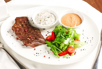 Meat steak beef with fresh vegetables, herbs and two kinds of sauces on white dish