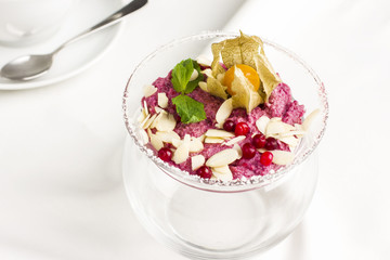 Pink raw dessert mousse ice cream with berries and nuts in glass jar on white table