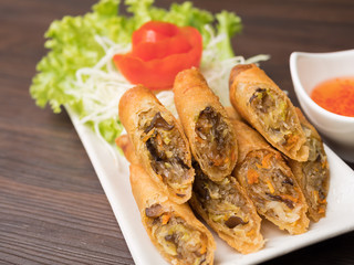 Close up of a fried spring roll on white plate with sweet sauce and fresh vegetable