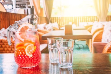 Pitcher with orange juice and two empty mugs stand on a table in a cafe on a hot, sunny day. Copy space for text.