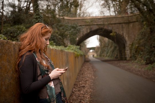 Woman using cell phone while leaning against wall