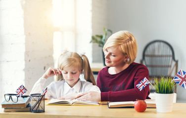 Female educator of English and smart girl, working table with books, british flag and apple, kids...