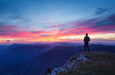 A hiker is looking at a pink sunset in a mountainous wilderness.