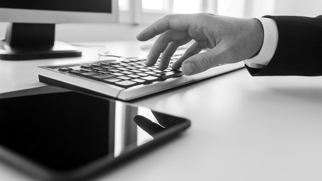 Monochrome image of businessman typing on a computer keyboard in office