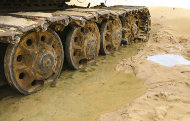 old iron caterpillar in wet sand. Rusty steel wheels and caterpillar tape of a large  bulldozer, tank, excavator, in damp sand and puddles.