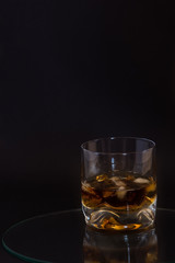 Glass of brandy served with ice on dark background