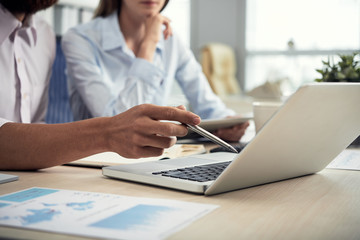 Faceless shot of man and woman sitting at table in office using laptop and having project discussion