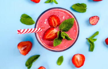 A glass of strawberry smoothie with mint on a blue background. Nearby lie pieces of strawberries and mint leaves.