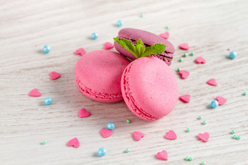 Strawberry and blueberry macaroons, a mint leaf and a sweet poppy lie on a white wooden background.