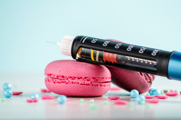 Two strawberry macaroons, a sweet powder and an insulin pen lie on a white wooden table on a blue...