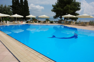 View of the blue pool and white umbrellas in modern Greek hotel.