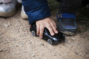 The child's hand holds a black toy car. Children play in the street.