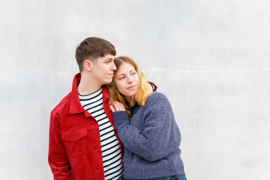 young affectionate couple standing in front of concrete cement wall loooking towards copy space