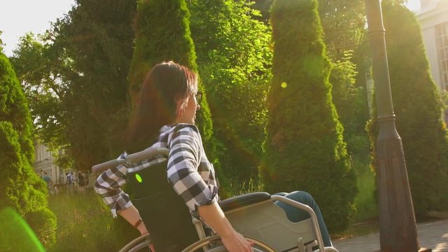 Disabled girl in a shirt in a wheelchair rides through the Park at sunset.Slow mo