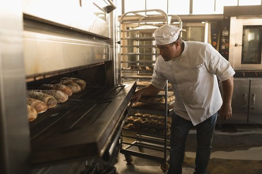Male baker using baking owen in bakery shop