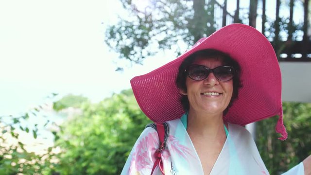 Happy mature woman in pink hat and sunglasses in tropical resort on vacation time. slow motion. 3840x2160