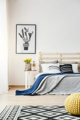 Black and white cactus poster hanging on the wall in bright bedroom interior with yellow fresh flowers, double bed and patterned carpet