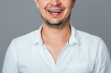 Crop portrait of cheerful handsome young man in white shirt smiling while standing against grey isolated background. People Emotions Lifestyle Fashion Business concepts