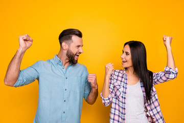 Portrait of joyful successful couple with raised arms looking at each other yelling celebrating achievement isolated on bright yellow background