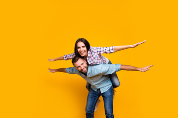 Low angle view portrait of playful foolish couple making air plane holding hands to the side looking at camera isolated on vivid yellow background