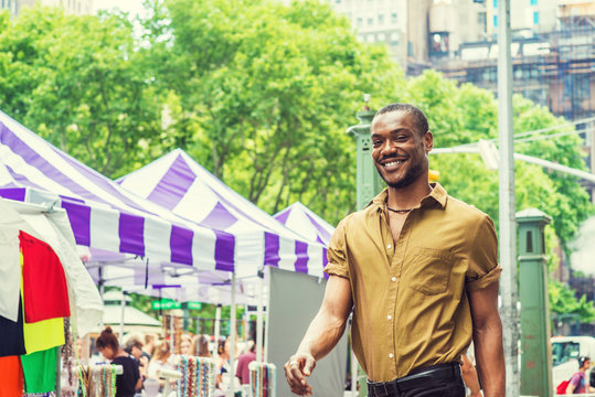 Summer Street Fair and Flea Market in New York. Young African American Man shopping, traveling in New York, wearing green short sleeve shirt, walking by street in Midtown of Manhattan, smiling..