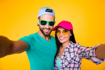 Self portrait of stylish trendy students in modern eyeglasses colorful headwear shooting selfie on front camera having beaming smiles isolated on bright yellow background