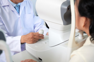 Crop shot of doctor controlling special machine while examining eyesight of patient working at oculist in hospital  - obrazy, fototapety, plakaty